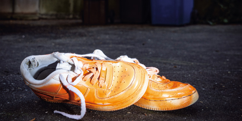 Ein Paar ramponierte, orangefarbene Sneaker mit offenen Schnürsenkeln liegt auf Asphalt
