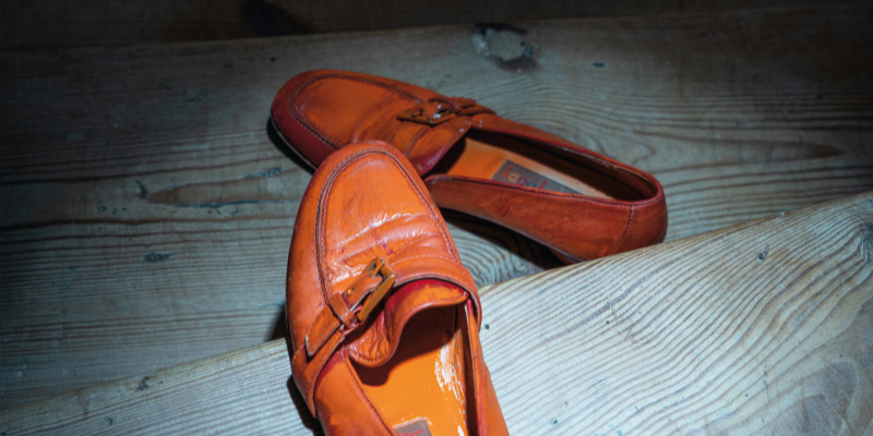 Ein Paar orangefarbener Loafer liegt auf einer Holztreppe